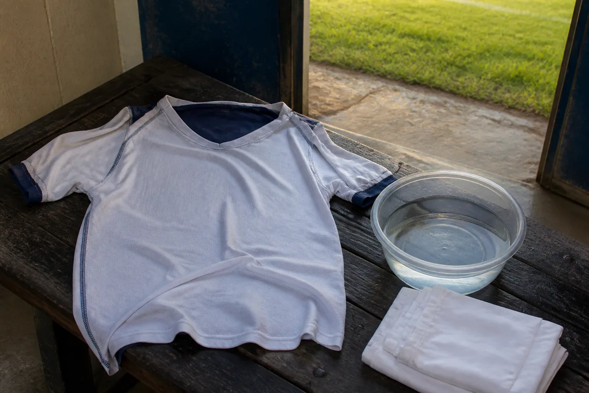 Gros plan sur une main tamponnant une tache avec un linge blanc sur un maillot de sport